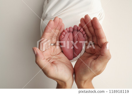 The palms of the parents. A father and mother hold the feet of a newborn child in a white blanket on a white background.. The feet of a newborn in the hands of parents. Photo of foot, heels and toes The palms of the parents. A father and mother hold the feet of a newborn child in a white blanket on a white background.. The feet of a newborn in the hands of parents. Photo of foot, heels and toes 118918119