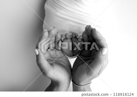 The palms of the parents. A father and mother hold the feet of a newborn child in a blanket. The feet of a newborn in the hands of parents. Black and white Photo of foot, heels and toes The palms of the parents. A father and mother hold the feet of a newborn child in a blanket. The feet of a newborn in the hands of parents. Black and white Photo of foot, heels and toes 118918124