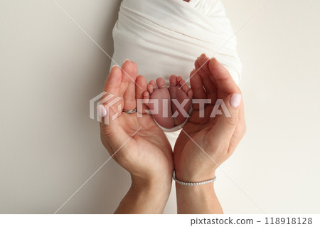 The palms of the parents. A father and mother hold the feet of a newborn child in a white blanket on a white background.. The feet of a newborn in the hands of parents. Photo of foot, heels and toes The palms of the parents. A father and mother hold the feet of a newborn child in a white blanket on a white background.. The feet of a newborn in the hands of parents. Photo of foot, heels and toes 118918128