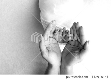 The palms of the parents. A father and mother hold the feet of a newborn child in a blanket. The feet of a newborn in the hands of parents. Black and white Photo of foot, heels and toes 118918131
