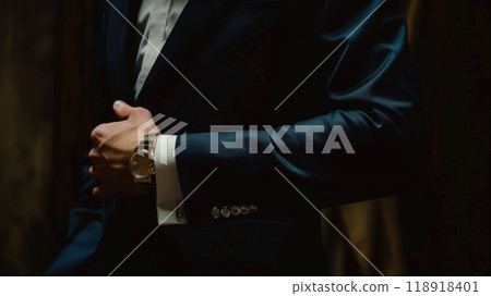Stylish Businessman Adjusting Cufflink in Navy Suit on Moody Background 118918401