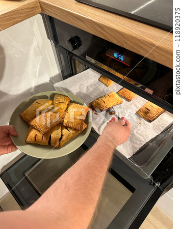 Freshly baked pastries are being taken out of the oven, steaming and golden brown, ready to be served on a green plate. Aroma of crispy dough fills the cozy kitchen, evoking a sense of warmth and 118920375