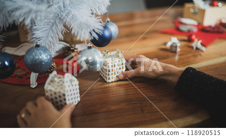 Closeup view of female hands preparing a holiday setting by placing small christmas gift boxes under a white tree 118920515