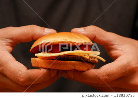 Ready to eat tasty fast food hamburger. Unhealthy food concept. Hands holding homemade beef burger on wooden table. Man holds burger with hands. Home delivery. Close up shot of young man eats burger. 118920753