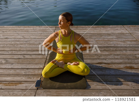 A Woman Engaging in Yoga Practice Wearing a Bright Yellow Outfit by the Serene Water 118921581