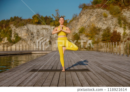 Experience a serene yoga pose on a beautiful scenic dock surrounded by vivid autumn colors 118921614