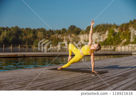 A dynamic yoga pose by the water in vibrant attire, blending energy and grace, captivating viewers A dynamic yoga pose by the water in vibrant attire, blending energy and grace, captivating viewers 118921616