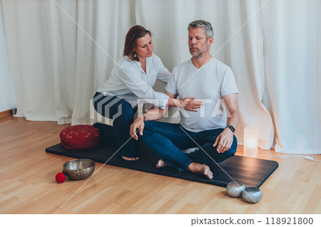 Man and woman practicing mindful breathing together during a meditation session,seated on mats with sound bowls Man and woman practicing mindful breathing together during a meditation session,seated on mats with sound bowls 118921800