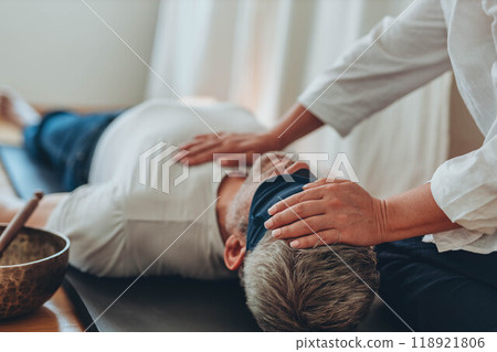 A man lying on a mat with a blindfold, practicing breathing exercises while a woman acts as a coach, assisting him A man lying on a mat with a blindfold, practicing breathing exercises while a woman acts as a coach, assisting him 118921806