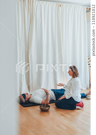 A man lying on a mat with a blindfold, practicing breathing exercises while a woman acts as a coach, assisting him A man lying on a mat with a blindfold, practicing breathing exercises while a woman acts as a coach, assisting him 118921812