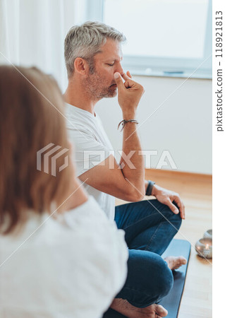 A man sitting in lotus position and a woman practicing alternate nostril breathing exercises during a meditation session 118921813