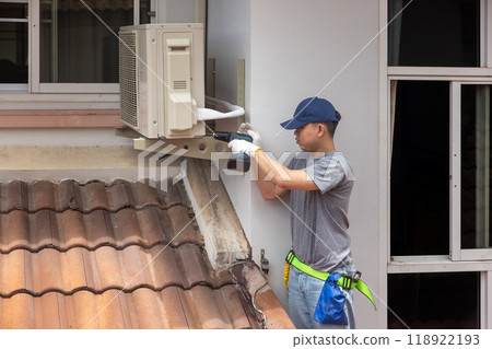 Technician fixing air conditioner unit on outside wall. Technician fixing air conditioner unit on outside wall. 118922193