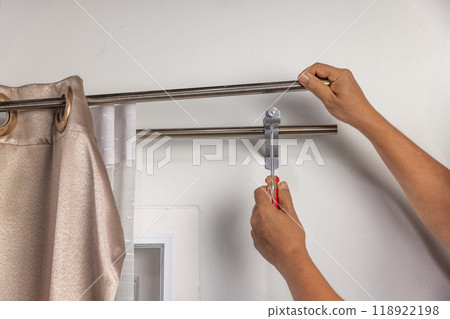 Worker repairman hanging and fixing the curtain on the window Worker repairman hanging and fixing the curtain on the window 118922198