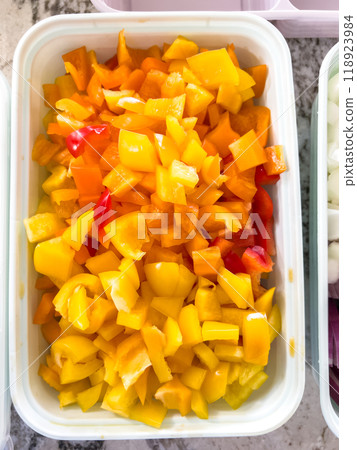 Chopped Vegetables in Containers Ready for Cooking on a Marble Countertop. High quality photo A variety of chopped vegetables, including yellow bell peppers, red onions, and white onions, are neatly 118923984