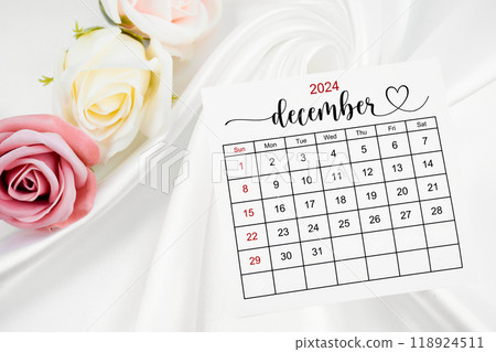 December 2024 calendar page and rose flower on white satin textile. 118924511