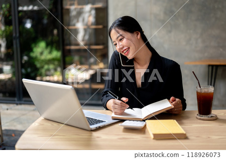 Attractive, busy Asian businesswoman is multitasking, talking on the phone while working at her desk Attractive, busy Asian businesswoman is multitasking, talking on the phone while working at her desk 118926073
