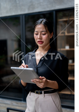 Professional Asian businesswoman is focused on reading her work on her digital tablet in her office. 118926103