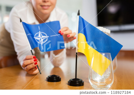 Unrecognizable girl sets midget flags of Ukraine and NATO before international negotiations 118927184