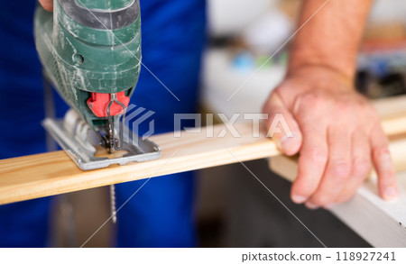 Closeup of hands using a jigsaw machine on wooden plank at the workshop, banner 118927241