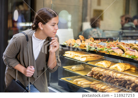 Smiling female tourist inspecting sandwiches through window of bakery Smiling female tourist inspecting sandwiches through window of bakery 118927253