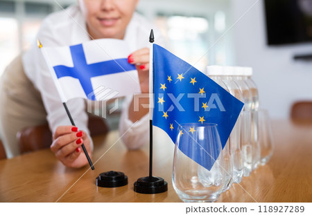 Female secretary places flags of the Finland and European Union flag on the table before negotiations of top political figures Female secretary places flags of the Finland and European Union flag on the table before negotiations of top political figures 118927289