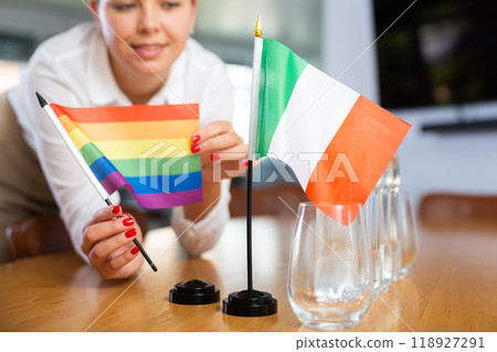Young woman putting LGBT and Italy flags on table in office 118927291
