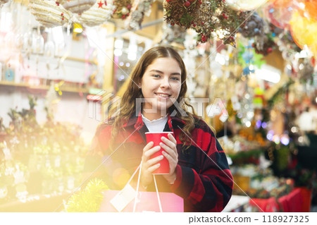 Happy girl with paper cup of coffee walking in Christmas fair Happy girl with paper cup of coffee walking in Christmas fair 118927325