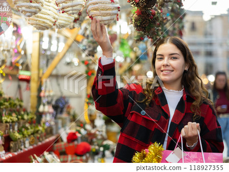 Girl in a plaid coat choosing handmade Christmas decorations at fair 118927355