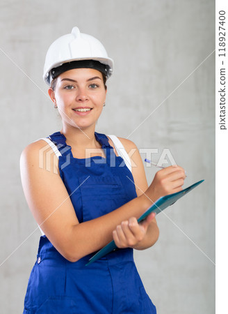 Young woman in work overalls making notes Young woman in work overalls making notes 118927400