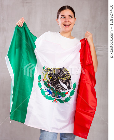 Joyous young woman holding Mexico flag against unicoloured background 118927410