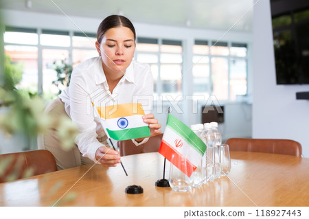 Positive young woman putting little flag of India on table next to the flag of Iran 118927443