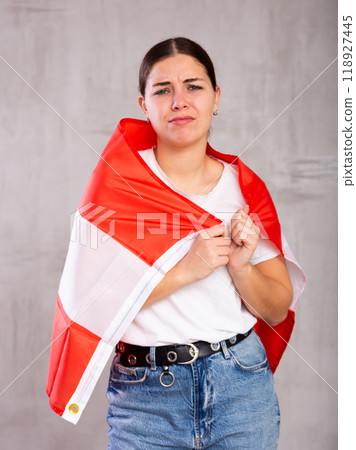 Sad young woman holding Austria flag against unicoloured background Sad young woman holding Austria flag against unicoloured background 118927445