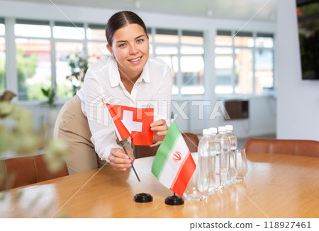 Positive young woman putting little flag of Switzerland on table next to the flag of Iran 118927461