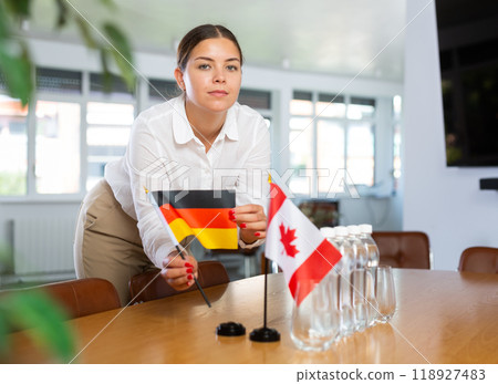 Young woman puts flags of Germany and Canada on table in office 118927483