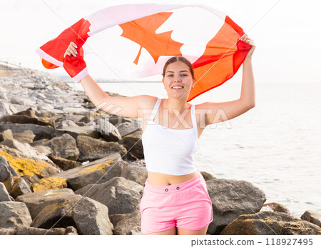 Slender girl with the flag of Canada on the seashore on sunny summer day Slender girl with the flag of Canada on the seashore on sunny summer day 118927495