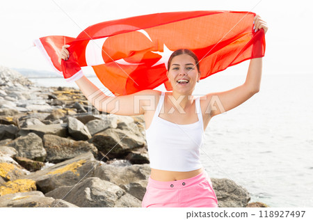 Enjoying vacation in Turkey. Young woman with national Turkish flag on the seashore on sunny day 118927497