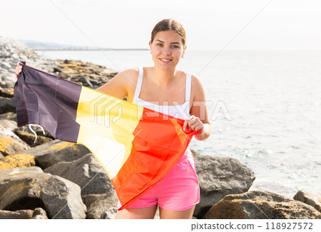 Portrait of happy woman of Belgium match waving a national flag on the seashore on sunny day 118927572