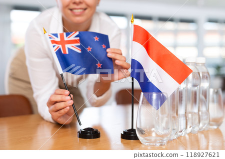 Woman secretary prepares an office for negotiations - she places flags of Netherlands and Australia table Woman secretary prepares an office for negotiations - she places flags of Netherlands and Australia table 118927621