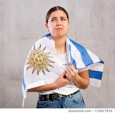 Sad young woman with flag of Uruguay against gray background indoors Sad young woman with flag of Uruguay against gray background indoors 118927654