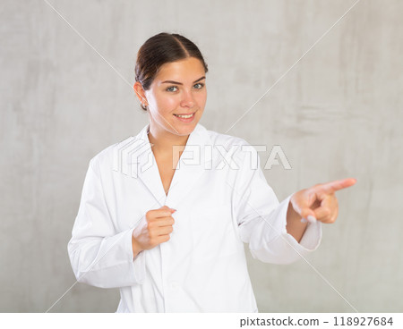 Happy young female doctor pointing to side with her finger Happy young female doctor pointing to side with her finger 118927684