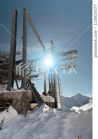 An unfinished metal structure of a cable car station high in the mountains. The structure is covered in snow and the sun shines through its ceilings 118929377
