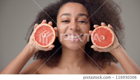 Beauty, vitamins and healthcare concept - beautiful African American woman with curly afro hairstyle and clean, healthy skin holds grapefruit halves in her hands and smiles with a bright toothy smile 118930306