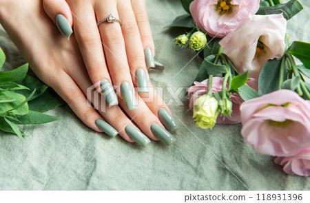 Elegant hands with green nail polish resting on a soft fabric surrounded by delicate flowers  118931396