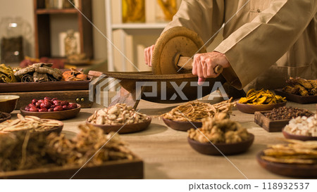 A traditional medicinal practitioner grinds herbs with a traditional mill. A sample photo for a traditional laboratory depicts a table with several sorts of dried herbs used in traditional medicine. 118932537