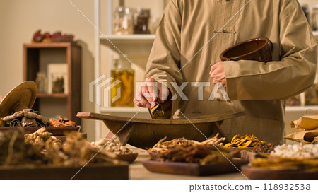 Image template with a classic medicine room backdrop showcasing a doctor uses a traditional wooden mill to gently ground herbal leaves while surrounded by dried herbs used in traditional medicine. Image template with a classic medicine room backdrop showcasing a doctor uses a traditional wooden mill to gently ground herbal leaves while surrounded by dried herbs used in traditional medicine. 118932538
