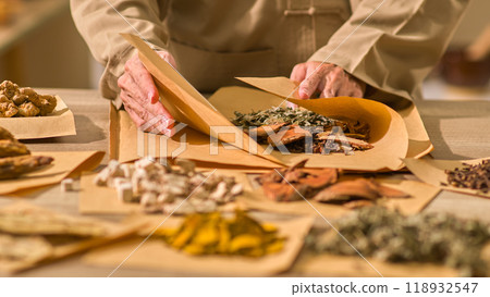 The traditional oriental healthcare zone shows a traditional medicine through that meticulously wraps paper that contains herbs. Brown pillow paper is also placed next to the plants. 118932547