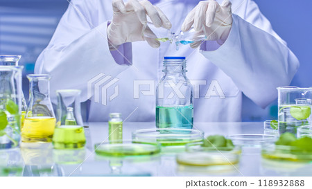 Scientist pouring two solution from two small bottle in hand into bottle containing blue solution fixed on stand. Quality image with modern laboratory setting. 118932888