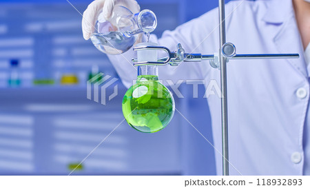 Scientist filling a flask with colored solution that is set on a stand with clear solution from the flask in their hand. high-quality photo in a contemporary lab environment. Scientist filling a flask with colored solution that is set on a stand with clear solution from the flask in their hand. high-quality photo in a contemporary lab environment. 118932893