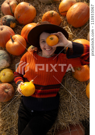 Woman lying on hay with pumpkins during autumn 118933067