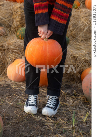 Person holding a large orange pumpkin by the stem 118933075
